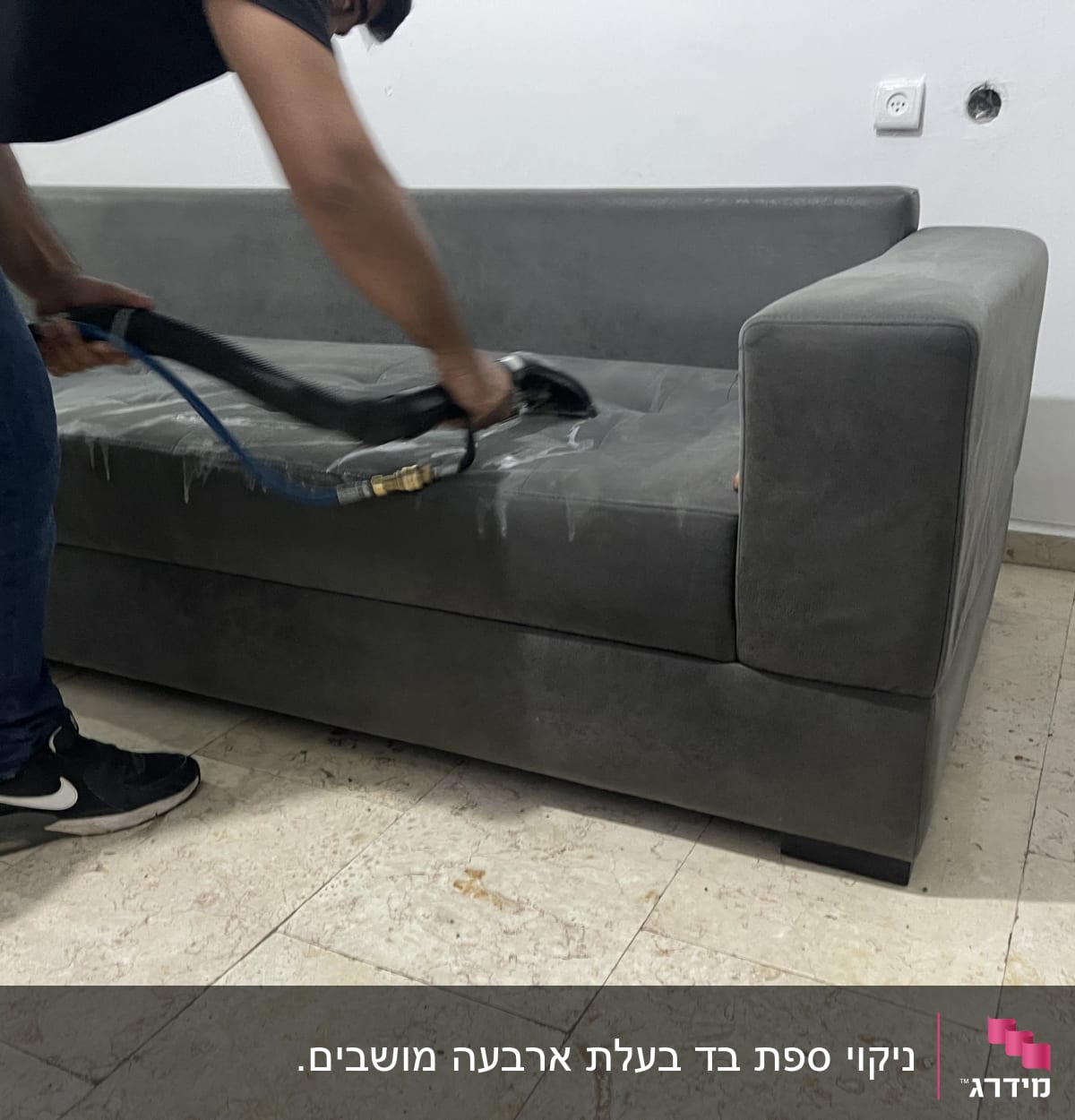 אדם מנקה ספה אפורה עם מכשיר ניקוי